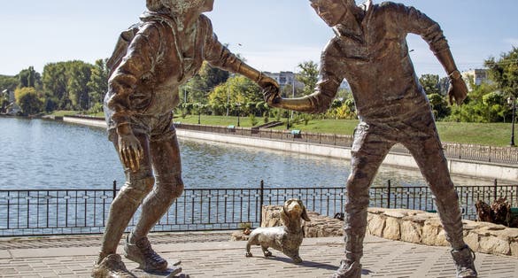 photo of Chisinau, Moldova-October 2, 2018: Young couple on skateboard with Basset Hound dog sculpture by petru glavan in valea morilor park.
