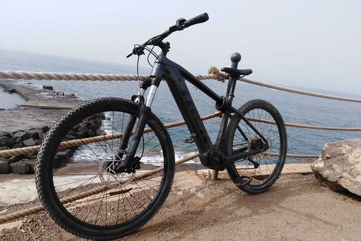 A black mountain bike is parked against a rope fence on a coastal path, overlooking the ocean and rocky shore..jpg