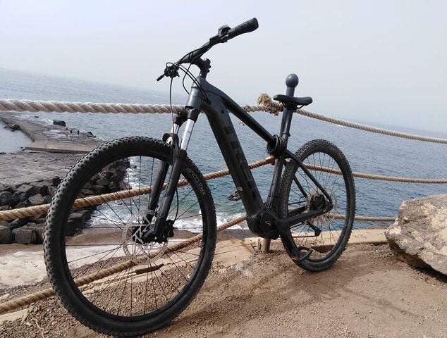 A black mountain bike is parked against a rope fence on a coastal path, overlooking the ocean and rocky shore..jpg