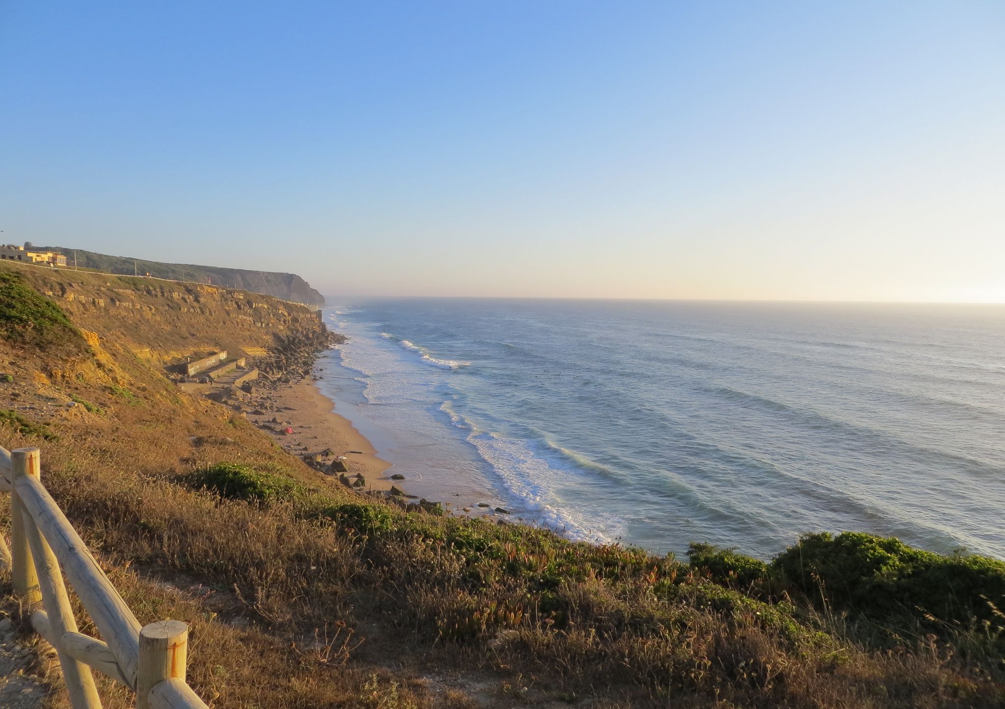 Photo of Cliff top view of Praia Grande from Praia Pequena do Rodízio, Sintra, Portugal. The waves of the Atlantic ocean. Taken on a sunny summer day.