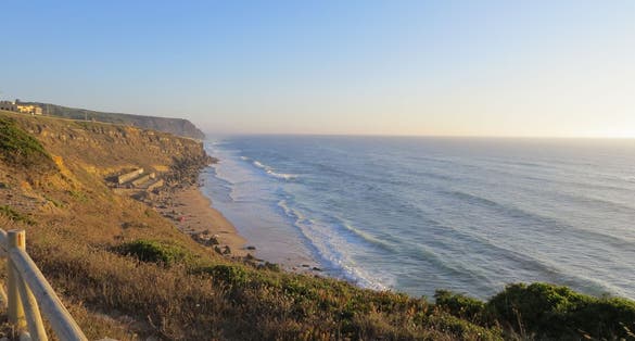 Photo of Cliff top view of Praia Grande from Praia Pequena do Rodízio, Sintra, Portugal. The waves of the Atlantic ocean. Taken on a sunny summer day.