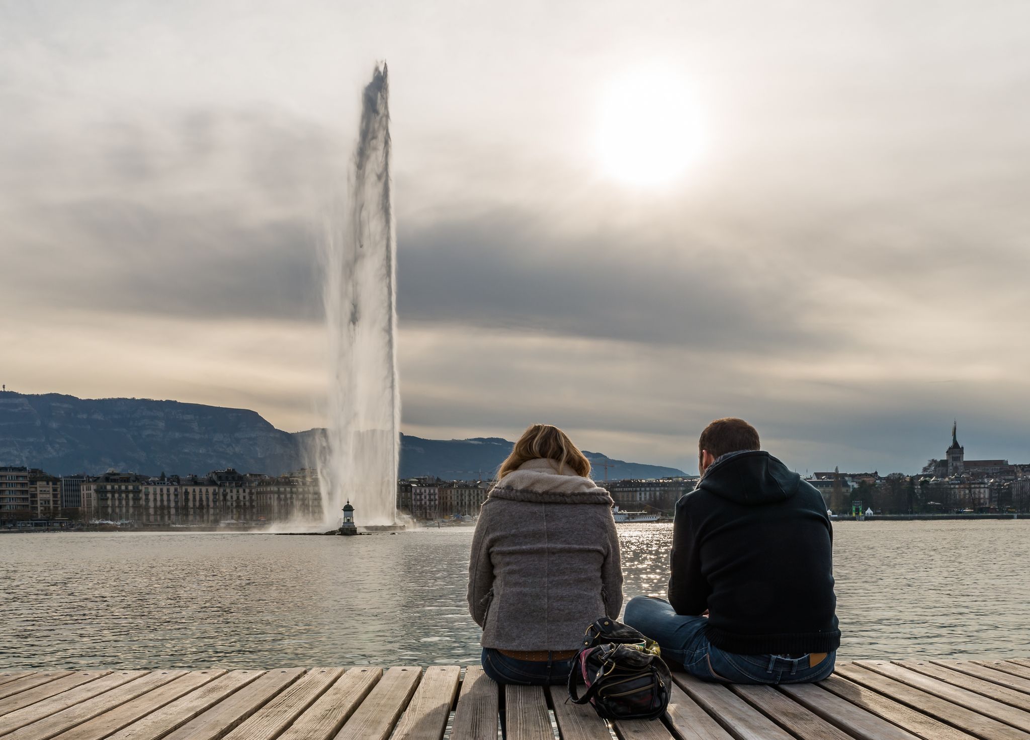 Photo of couple sitting on the wooden Jetty at Bains des Paquis, Switzerland.