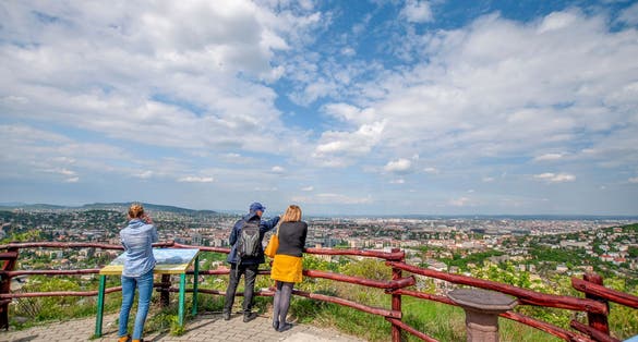Three people looking at the skyline of Buda and Pest from the Sas Hill viewpoint on a sunny day, Budapest