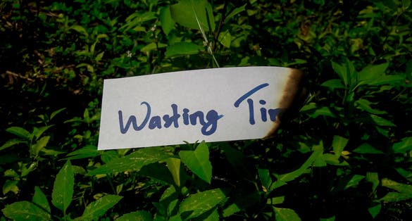 photo ofthe words wasting time on burning paper on green grass.