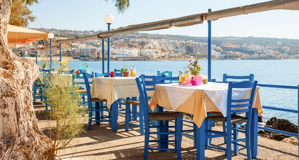 Photo of greek cafe terrace in Heraklion, Crete overlooking the sea with typical wooden chairs.