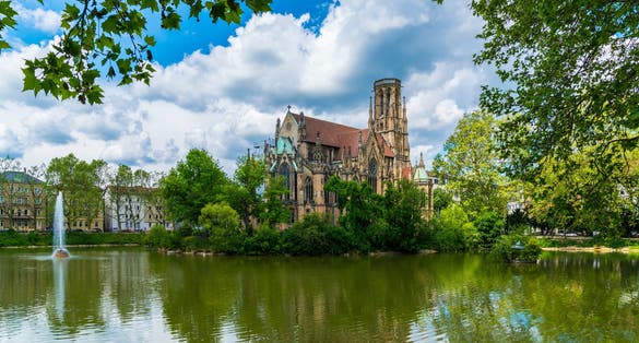 Photo of Germany, Stuttgart city downtown feuersee urban park st john church reflecting in lake water between green trees.