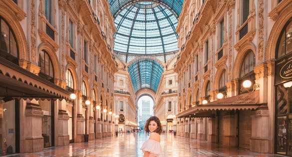 photo of Milan, Italy - August 12, 2018: An isolated girl in the middle of the galleria vittorio emanuele II in Milan with a pink dress and a straw hat.