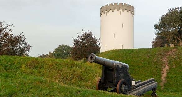 photo of view of Old white water tower on rampart in city Fredericia, Denmark.Old bronze cannon on rampart in city Fredericia, Denmark.