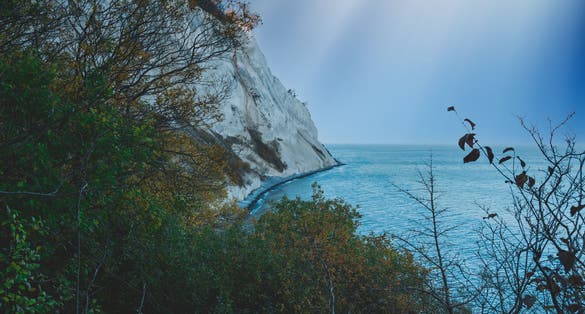Photo of Steep chalk cliffs going straight into an azure blue ocean for below at the famous Møns Klint in Denmark.