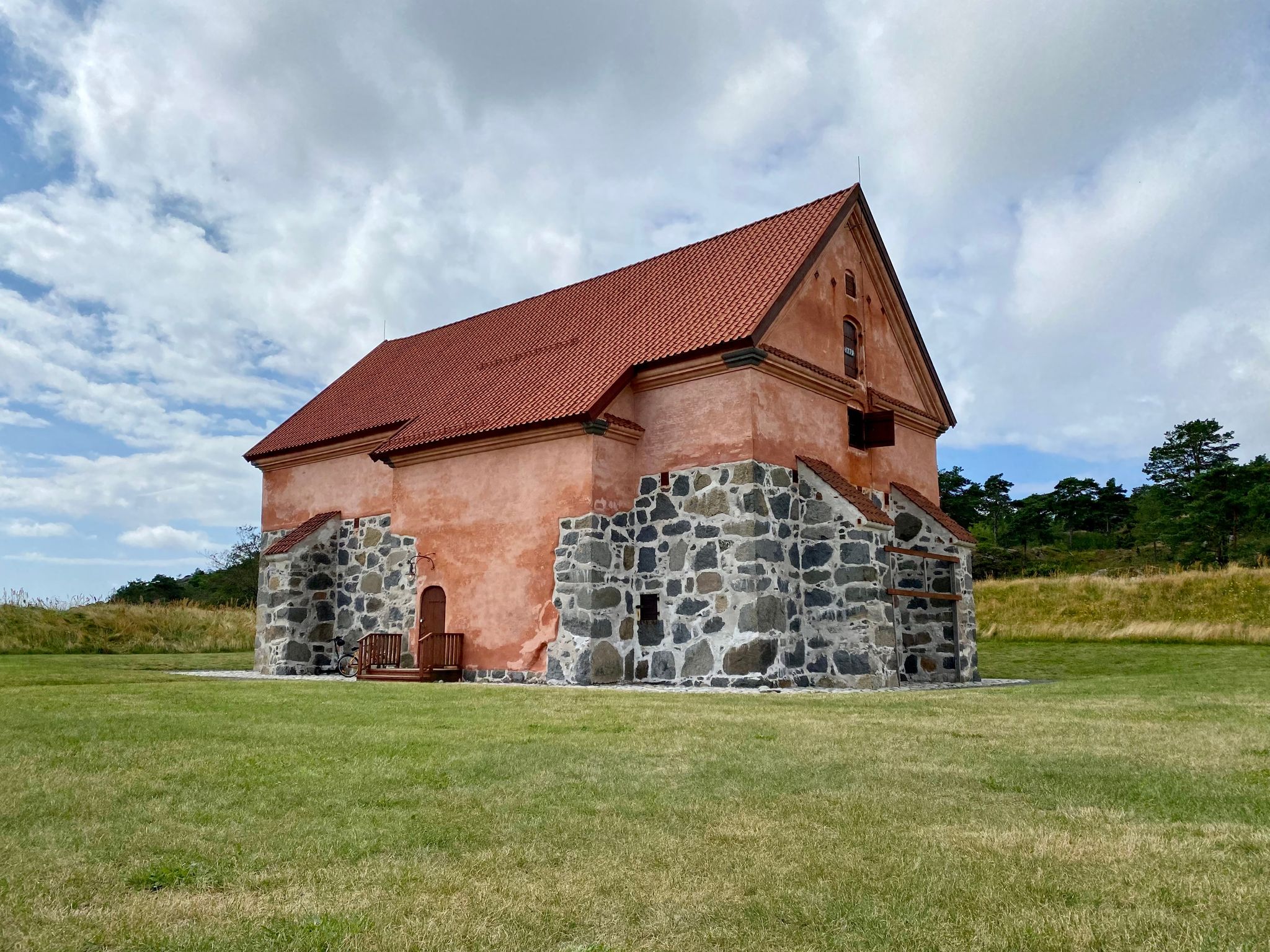 Old stone building with chipped orange paint on blue sky and green grass. This is a building called Krutthuset in Fredriksvern Verft in Stavern Norway.