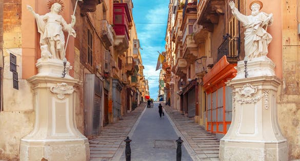 Photo of the traditional Maltese street stairs with corners of houses, decorated with statues of saints St. John and St. Paul and building with colorful balconies in Valletta, Capital city of Malta.