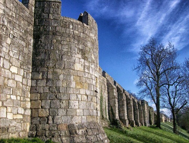 The ancient stone walls of York stand tall on a sunny day, with a tree and blue sky in the background..jpg