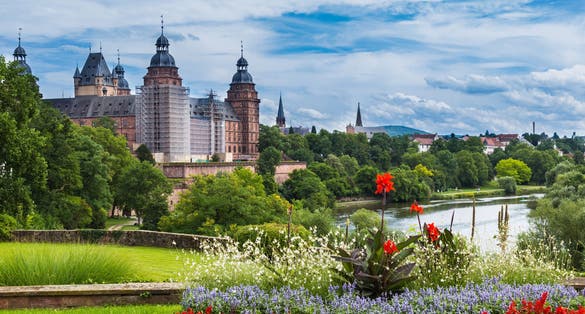 photo off view of Beautiful view of the old town Aschaffenburg, Germany and the palace Johannisburg on shore of river Main on the background of blue cloudy sky and green plants and flowers. Tourist attraction.