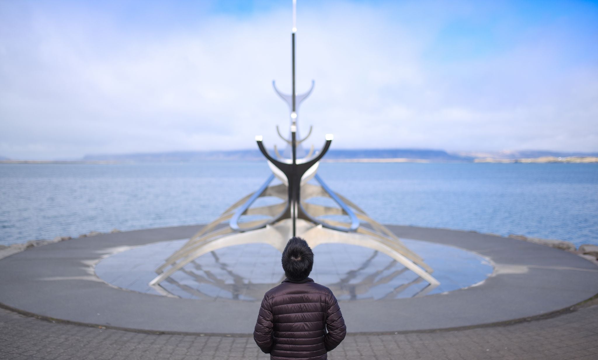 photo of sun voyager monument, Reykjavik, Iceland. A man was standing behind the sun voyager monument on the waterfront in Reykjavik, Iceland. This is the landmark of Reykjavik city.