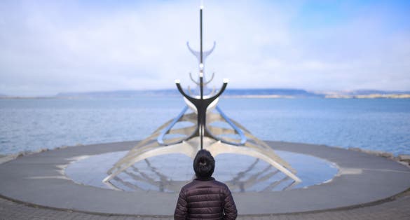 photo of sun voyager monument, Reykjavik, Iceland. A man was standing behind the sun voyager monument on the waterfront in Reykjavik, Iceland. This is the landmark of Reykjavik city.