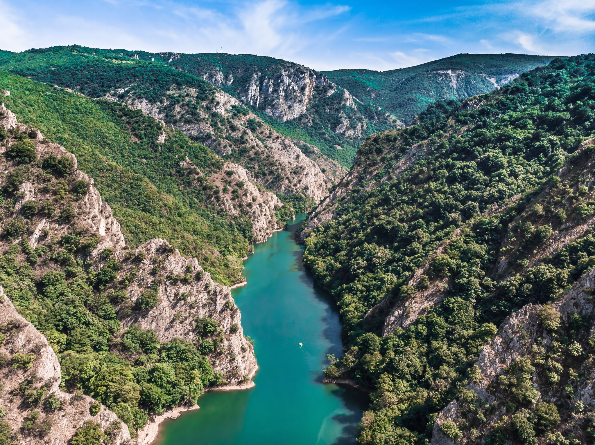 Drone view of Matka Canyon. Drone shot of a lake in a canyon in North Macedonia. Rocky green slopes. Transparent water surface of the lake. Mountain trail along the river. Lake in the mountains.