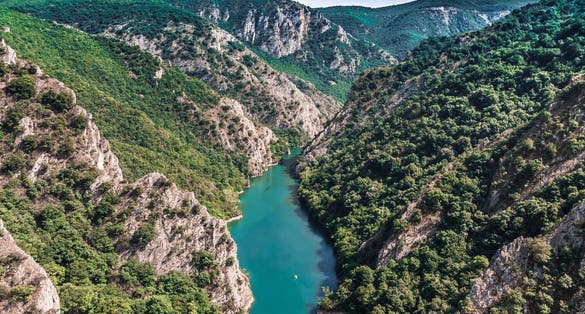 Drone view of Matka Canyon. Drone shot of a lake in a canyon in North Macedonia. Rocky green slopes. Transparent water surface of the lake. Mountain trail along the river. Lake in the mountains.