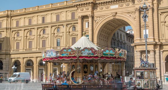 Vintage carousel and tourists in Piazza della Repubblica (Republic Square) and the arch in honor of the first king of united Italy on background in Florence, Italy.