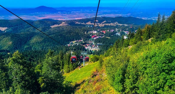 A view of red gondolas, and cableways moving to the top of the mountain over the beautiful landscapes around the Carpathian mountains in Poiana Brasov, Romania.