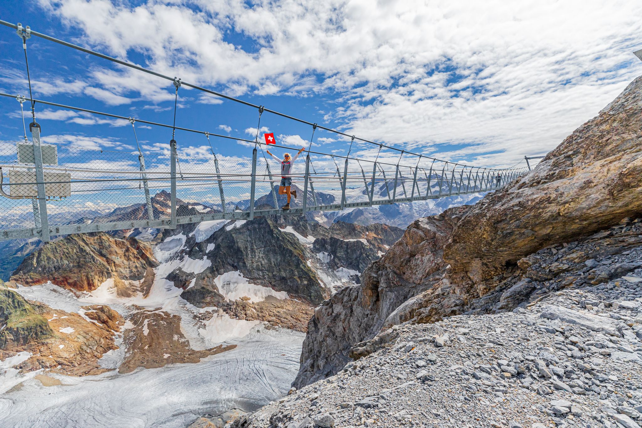 photo of woman on suspension bridge waving a Swiss flag. Titlis cliff walk with glacier in Switzerland. the highest suspension bridge in Europe.