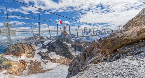 photo of woman on suspension bridge waving a Swiss flag. Titlis cliff walk with glacier in Switzerland. the highest suspension bridge in Europe.