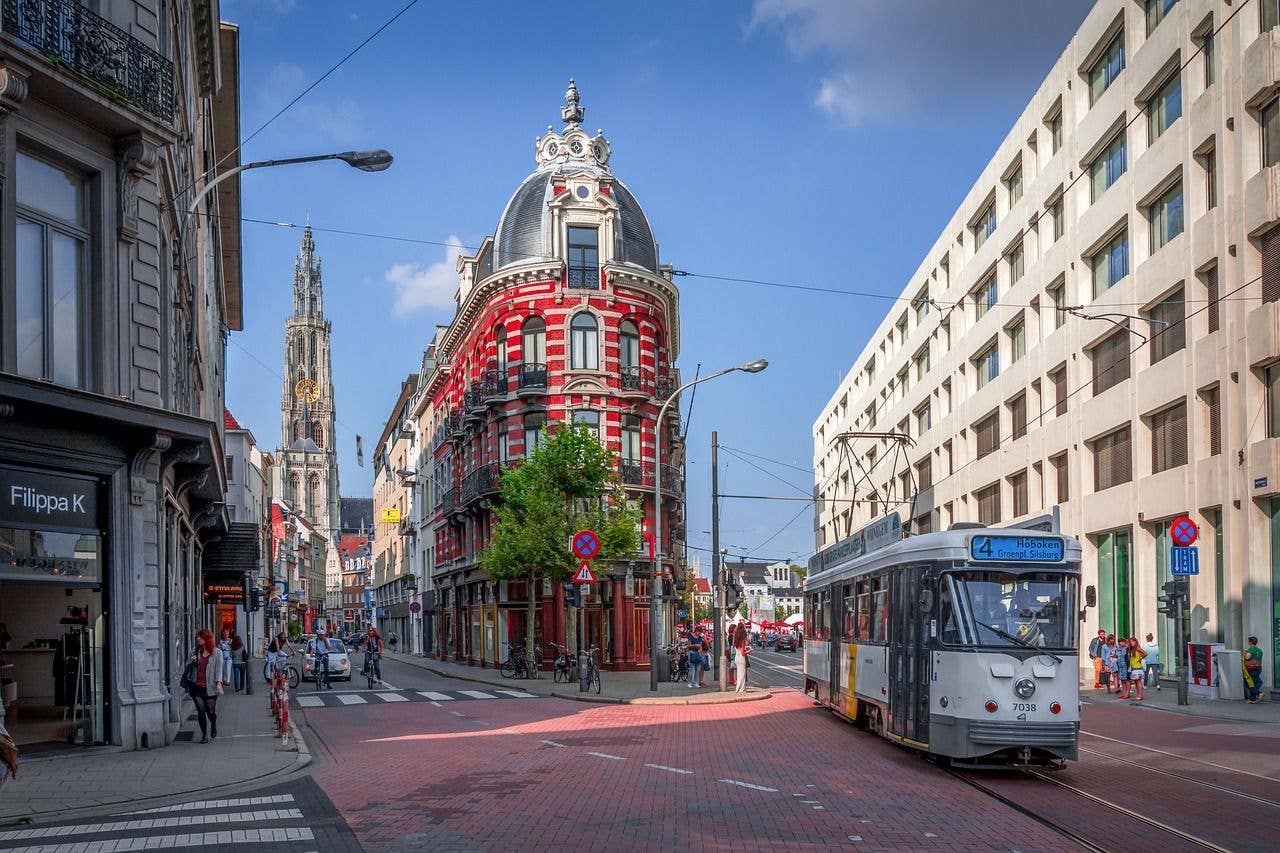 Charming Antwerp street with a historic red building, a passing tram, and the Cathedral of Our Lady in the background..jpg