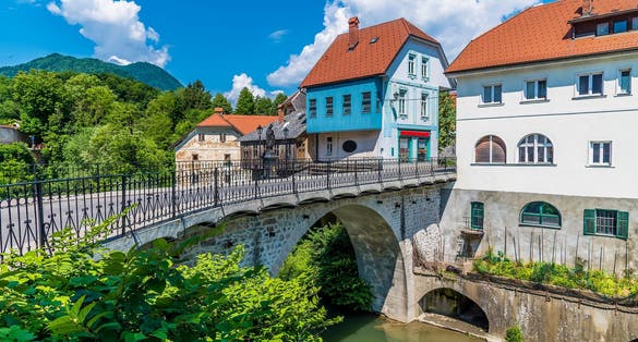 Photo of A view towards the fourteenth century Capuchin Bridge and buildings beside the Selca Sora River in Skofja Loka, Slovenia in summertime.