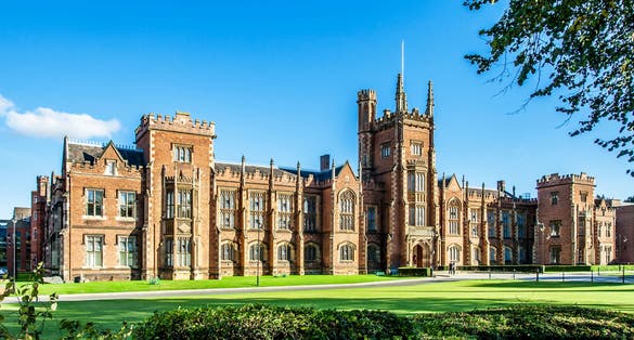 Photo of the Queen's University of Belfast with a grass lawn, tree branches and a hedge in sunset light.