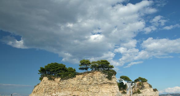 photo of view of Cameo Island, the most picturesque place in Laganas Bay, with pine trees growing in the rocks and white cloth blowing in the wind, Agios Sostis, Zakynthos, Greece,Laganas Greece.