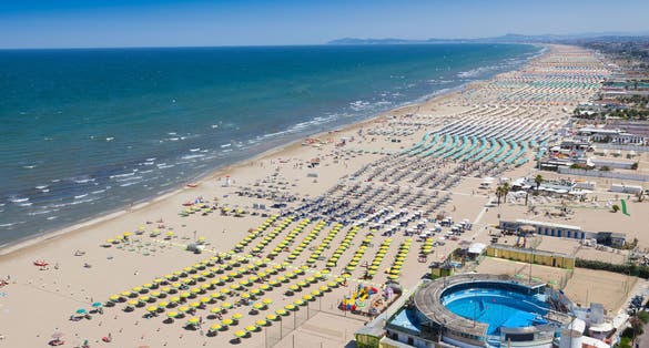 Photo of aerial view of umbrellas and chaise lounges on the beautiful beach of Rimini in Italy.