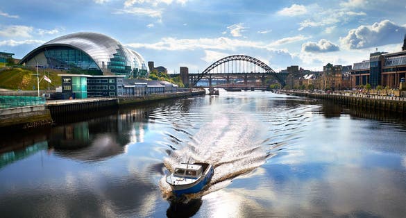 photo of view of A boat sailing down the River Tyne with Newcastle Tyne Bridge in the distance.