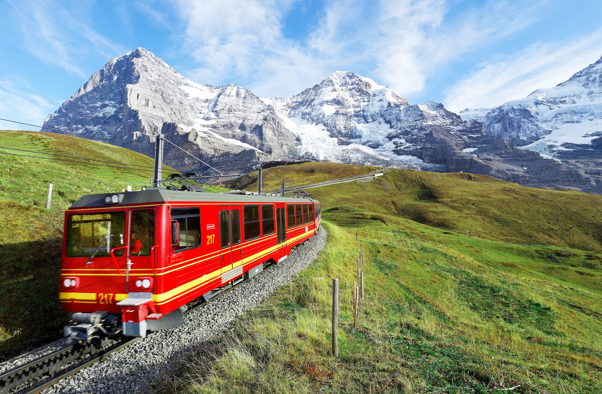 Photo of cogwheel train travels on the railway from Jungfraujoch (top of Europe) to Kleine Scheidegg on the green grassy hillside with Eiger, Switzerland.