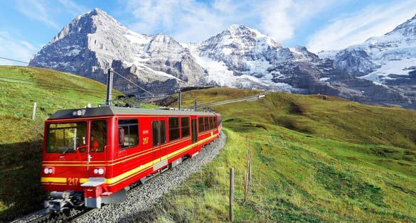 Photo of cogwheel train travels on the railway from Jungfraujoch (top of Europe) to Kleine Scheidegg on the green grassy hillside with Eiger, Switzerland.