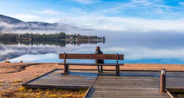 Woman sitting on a bench at a beach watching the nice view with mountain and river, Gällivare, Swedish Lapland, Sweden