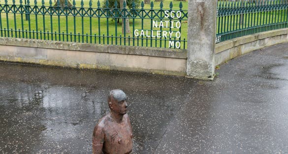 Sculpture of a man buried in the ground in front of the Scottish National Gallery of Modern Art in Edinburgh, UK. Edinburgh is the most popular tourist destination in Scotland.