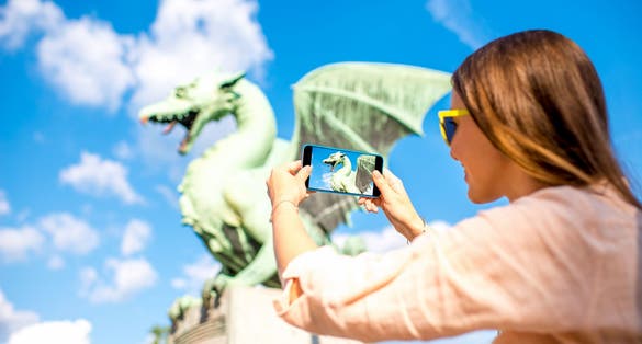 Young female traveler photographing with smart phone Dragon statue on the bridge in Ljubljana city. Dragon statue is one of the most famous symbols of the capital of Slovenia