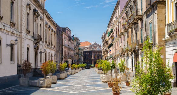 Via Teatro Massimo street with green plants trees leads to Massimo Bellini Opera House in Catania city, Sicily, Italy