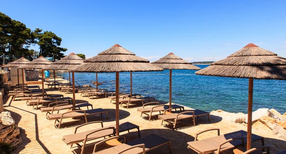 Photo of Beach and resort with beach chairs and umbrellas in morning light on the beach of a Croatian seaside holiday resort in Porec.