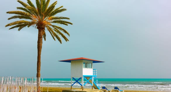 Photo of sandy beach with palm tree and life guard tower in Larnaca, Cyprus.