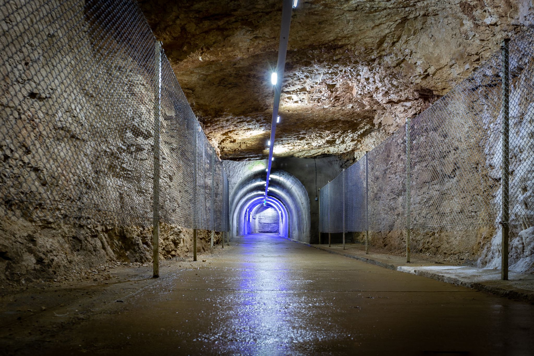 Photo of stone tunnel drilled underground in the rock with blue illuminations and protective fence, exit from Prometheus Cave Natural Monument in Georgia.