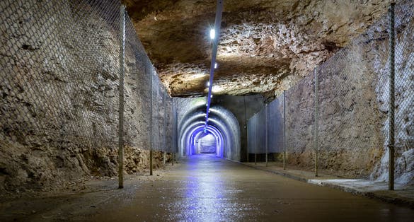 Photo of stone tunnel drilled underground in the rock with blue illuminations and protective fence, exit from Prometheus Cave Natural Monument in Georgia.