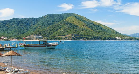 Photo of tourist boat moored at small pier at Icmeler beach with green hills at background in Aegean sea, Marmaris, Turkey.