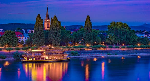 photo  of view of Skyline of Bonn, Germany. Beautiful night shot of great german city. Panorama with boat, trees, and historic architecture reflected in the water.