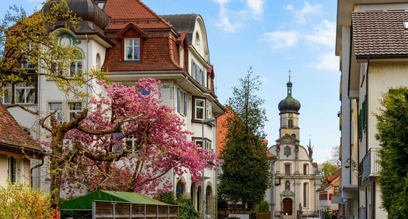 photo of view of A picturesque street in the city of St. Gallen with houses in traditional Swiss style among flowering trees, an ancient church in the background