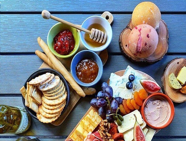 A wooden table with a colorful cheese board, crackers, fruit, jams, honey, and bread, ready for a meal..jpg