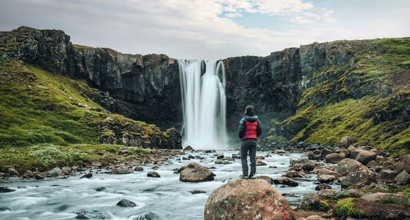 photo of view Beautiful view of Gufufoss waterfall flowing with young asian tourist woman standing on the rock in summer at Seydisfjordur, East of Iceland.