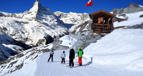 photo of skiers on the way to ski slope in Swiss Alps in sunny day, Zermatt, Matterhorn behind. Small wooden house with red swiss flag near by ski slope. Mountains and skiing resort photo manipulation, Switzerland.