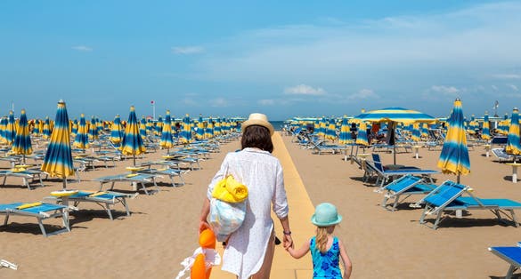 Photo of Woman and child outdoors. Mother and daughter going to rest on beach. Rimini, Italy.