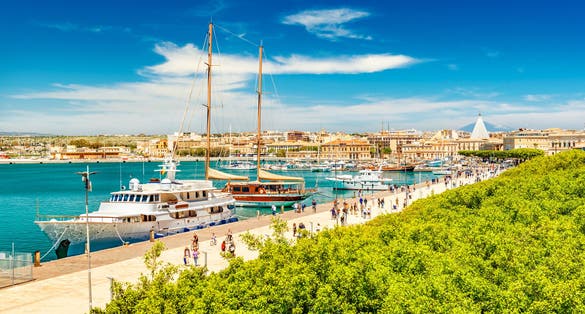 Beautiful view of the harbor in Syracuse with people walking along the promenade. Cityscape of Ortygia Island, Sicily, Italy