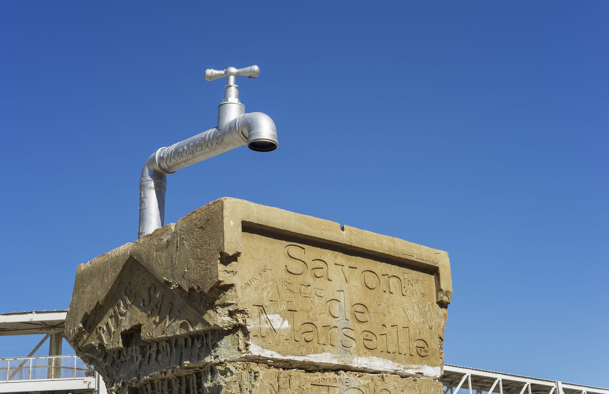 Art installation of a giant faucet on a carved block featuring -Savon de Marseille,- a tribute to the city’s famous traditional soap, under a clear blue sky.jpg